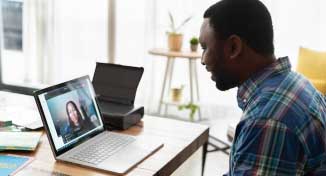 Image of Man sitting infront of a laptop having a virtual interview with a lady on screen.